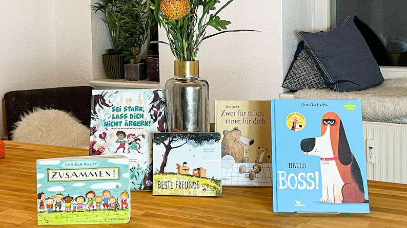 Ausgewählte Bücher werden mit einer Blumenvase im Hintergrund auf einem Tisch präsentiert.