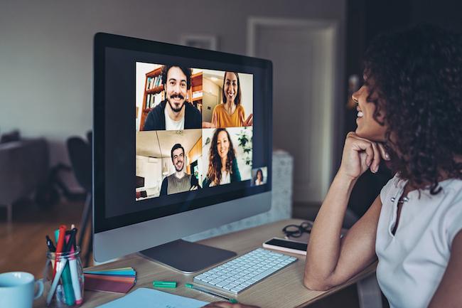 Junge Frau sitzt lächelnd vor einem Screen und reded mit Kolleg:innen in einem Webmeeting