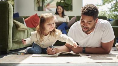 
		Vater sitzt mit seiner Tochter auf dem Wohnzimmerboden und plant Finanzen
	