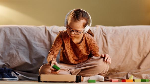 
		Kind mit Kopfhoerern sitzt auf dem Boden und spielt
	