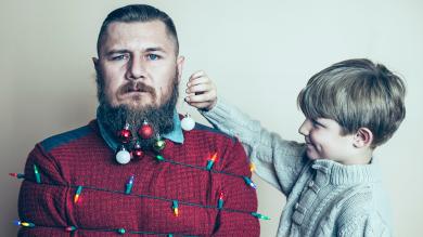 
		Junger Vater im Stress wird von Kind mit Weihnachtsdeko behängt
	