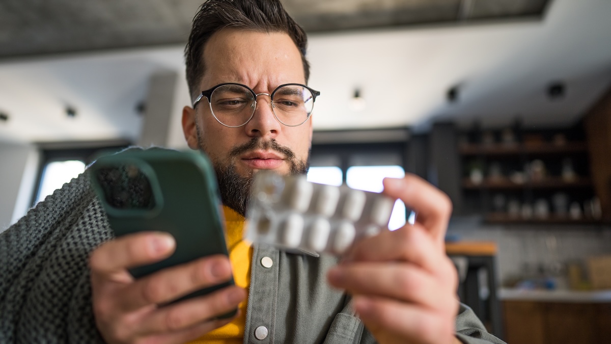 Kranker Mann mit Handy und Tabletten in der Hand