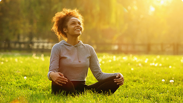 Eine junge Frau sitzt lächelnd in einer Wiese und macht Yoga